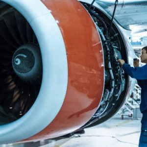 Aircraft maintenance mechanic with a flash light inspects plane engine in a hangar.