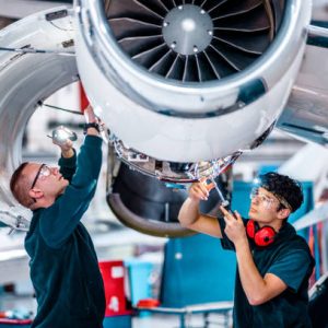 Two maintenance engineers checking and inspecting an airplane jet engine using the work tool in the hangar.